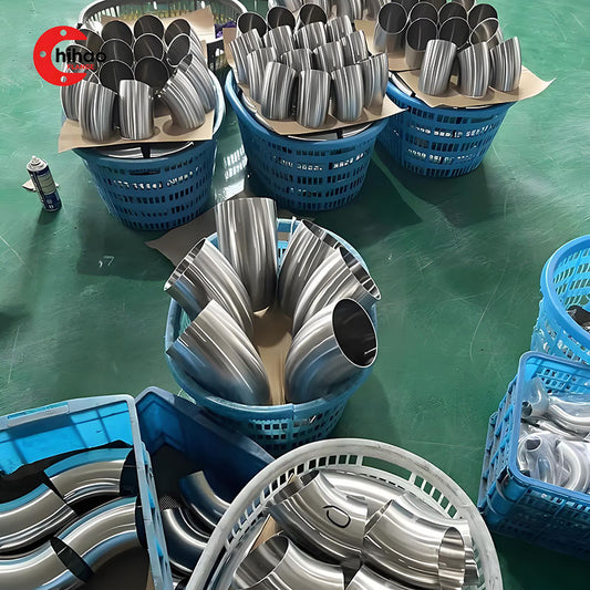 Sanitary stainless steel elbows bulk production in factory workshop, finished polished elbows stored in blue baskets for food, beverage and pharmaceutical pipeline applications.